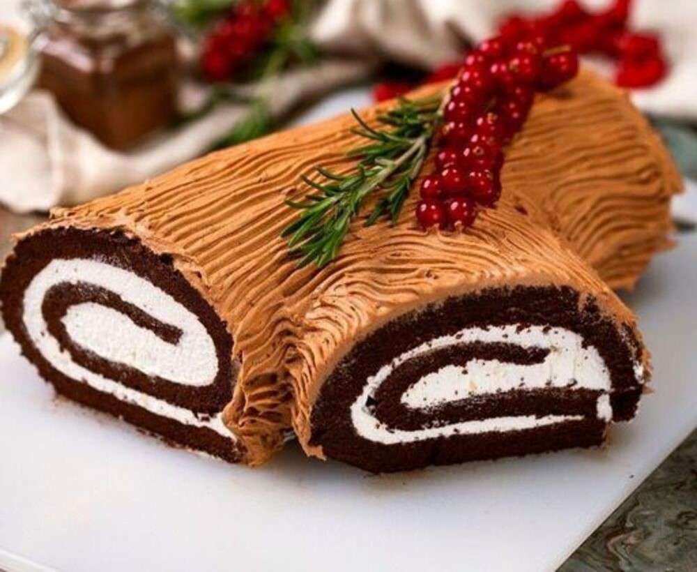 Bûche de Noël au chocolat décorée de groseilles rouges, brins de romarin et sucre glace.