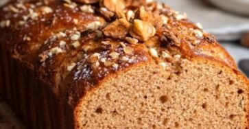 Pain d'épices de Noël doré avec une tranche coupée révélant des fruits confits et une texture moelleuse.