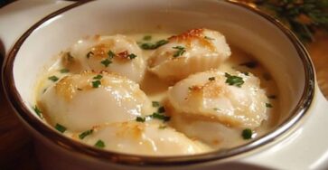 Gratin de Saint-Jacques à la crème avec fromage doré, servi dans un ramequin décoré de persil frais.