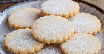 Sablés à la poudre d’amande joliment décorés avec du sucre glace, sur une assiette, prêts à être dégustés.