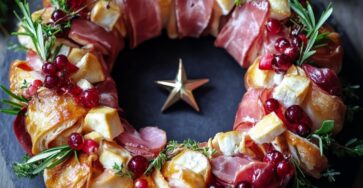 Couronne apéritive festive au fromage, jambon cru et herbes fraîches décorées de canneberges et romarin.