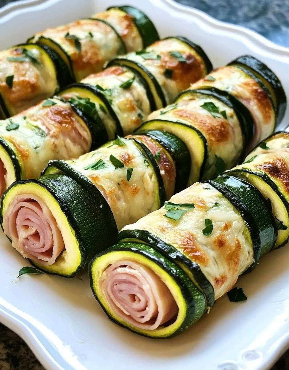 Roulés de courgettes au jambon et fromage ail et fines herbes, joliment disposés sur un plat de service, prêts à être dégustés.