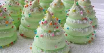 Meringues de Noël en forme de sapins verts, décorées avec des vermicelles colorés et des étoiles en sucre, présentées sur une assiette festive.