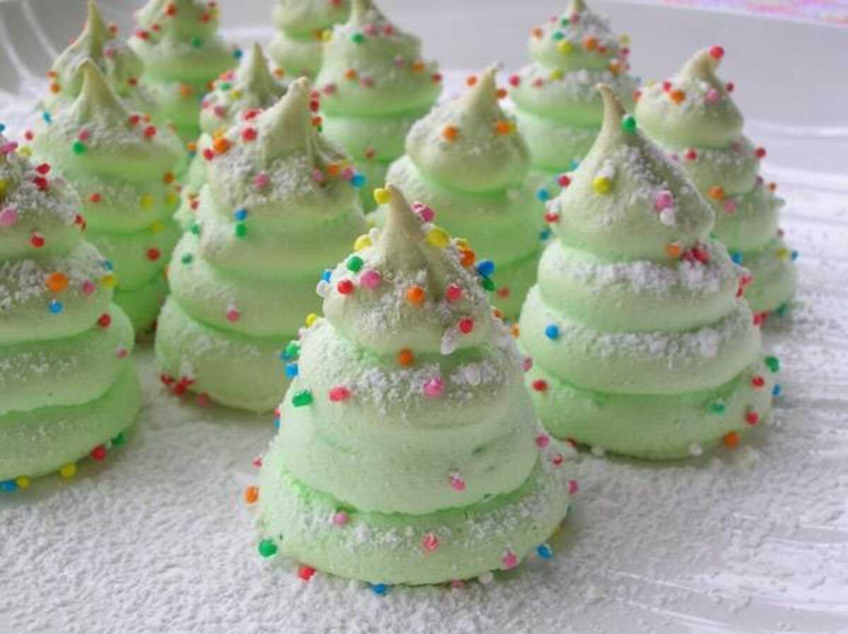 Meringues de Noël en forme de sapins verts, décorées avec des vermicelles colorés et des étoiles en sucre, présentées sur une assiette festive.