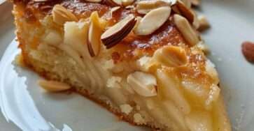 Gâteau au yaourt doré, garni d’amandes effilées et de morceaux de poires, servi sur une assiette avec une tasse de thé.