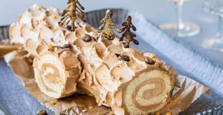 Bûche de Noël chocolat-moka, roulée et décorée de motifs en chocolat et de paillettes comestibles, présentée sur une table festive.