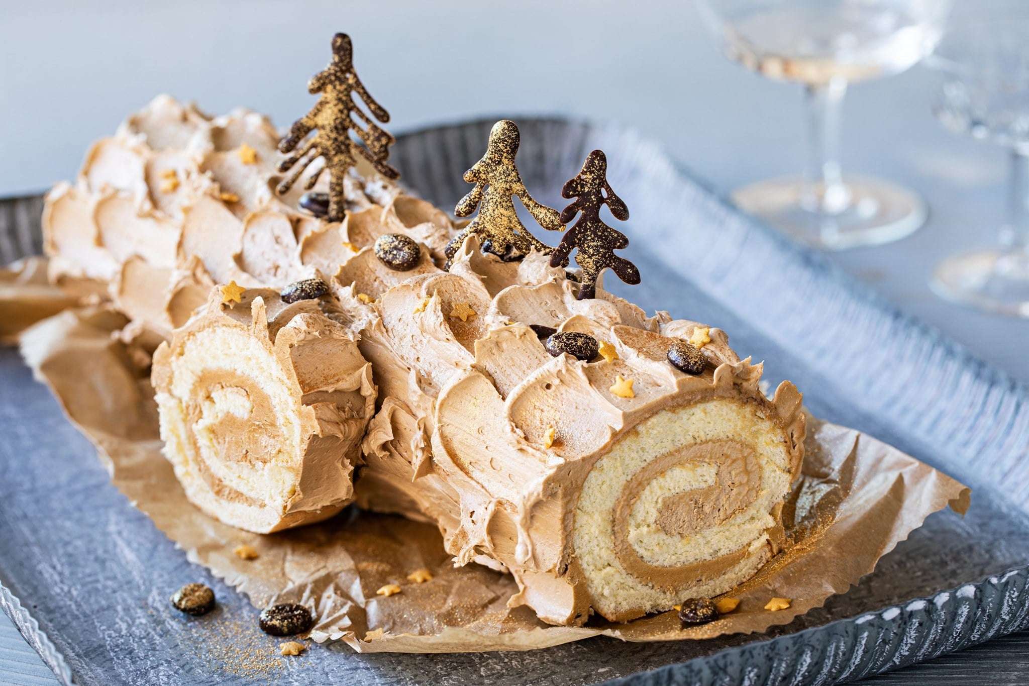 Bûche de Noël chocolat-moka, roulée et décorée de motifs en chocolat et de paillettes comestibles, présentée sur une table festive.