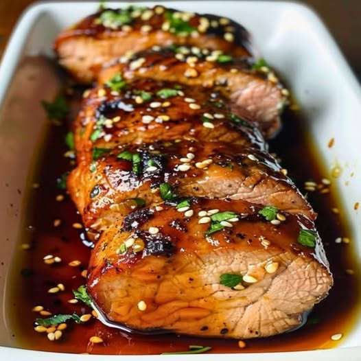 Filet de porc au miel et à l’ail, tranché en médaillons, nappé de glaçage doré et garni de persil frais, servi avec du riz et des légumes rôtis.