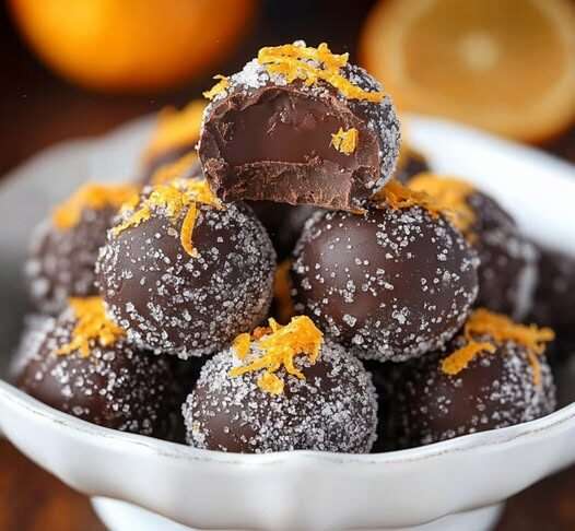 Truffes au chocolat noir roulées dans du sucre, garnies de zeste d’orange, disposées sur un plateau élégant pour une présentation festive.