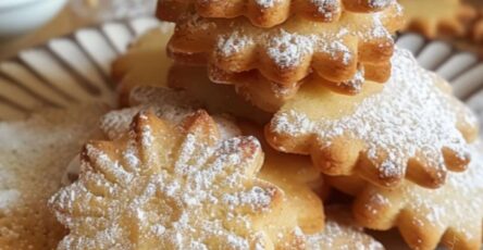 Une assiette de sablés maison dorés, saupoudrés de sucre glace, présentée sur une table avec des emporte-pièces et une tasse de thé.