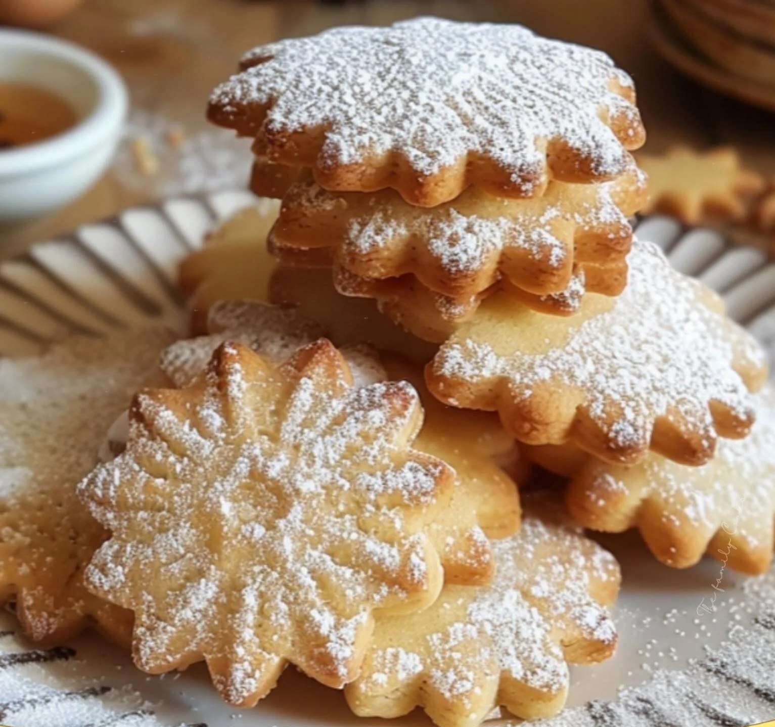 Une assiette de sablés maison dorés, saupoudrés de sucre glace, présentée sur une table avec des emporte-pièces et une tasse de thé.