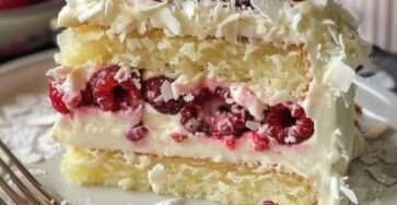 Gâteau roulé Forêt Blanche aux framboises et chocolat blanc, décoré de noix de coco râpée et de framboises fraîches.