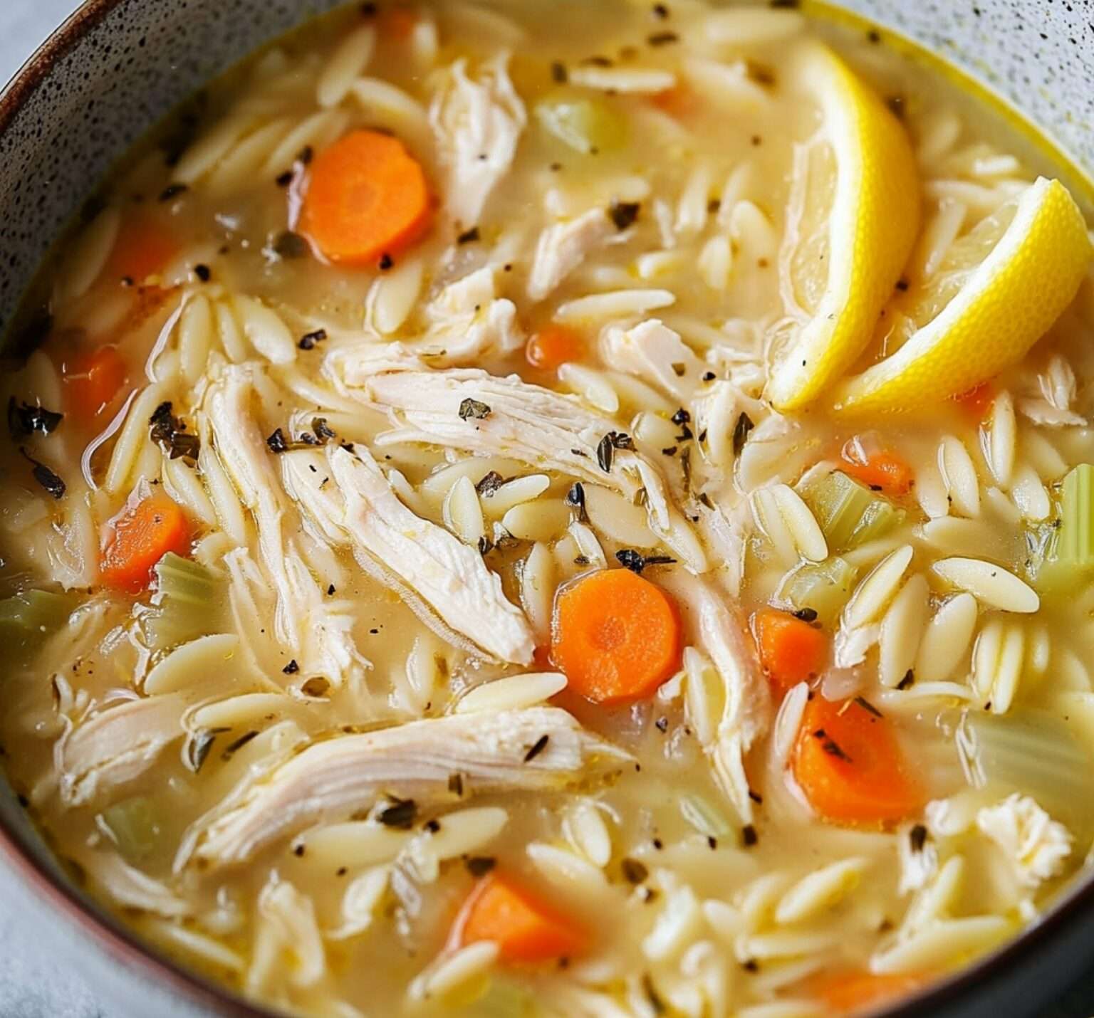 Un bol fumant de soupe au poulet et orzo au citron, garni de persil frais, avec des morceaux de légumes colorés et une texture crémeuse.