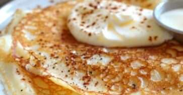 Crêpes dorées au fromage blanc sans farine, garnies de fruits frais et d’un filet de sirop d’érable, servies sur une assiette blanche avec des baies en décoration.