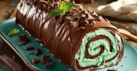 Bûche glacée menthe-chocolat, nappée de chocolat noir fondu, décorée de copeaux de chocolat et de feuilles de menthe fraîche, présentée sur un plat élégant.