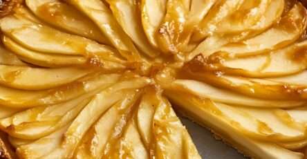 Une tarte fine aux pommes dorée, garnie de tranches de pommes finement disposées en rosace, servie sur une assiette élégante.