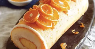 Une bûche Ensoleillée délicate et lumineuse, nappée d’un flocage orange, garnie de zestes de clémentines et posée sur une base croquante de pâte sablée.