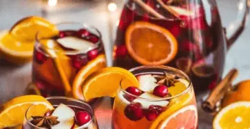 Verres de sangria de Noël sans alcool décorés avec des fruits, épices, et feuilles de menthe.