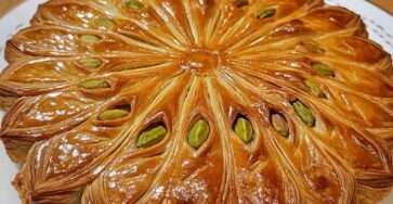 Une galette des rois dorée, garnie de crème de pistache onctueuse, décorée de pistaches concassées et saupoudrée de sucre glace.