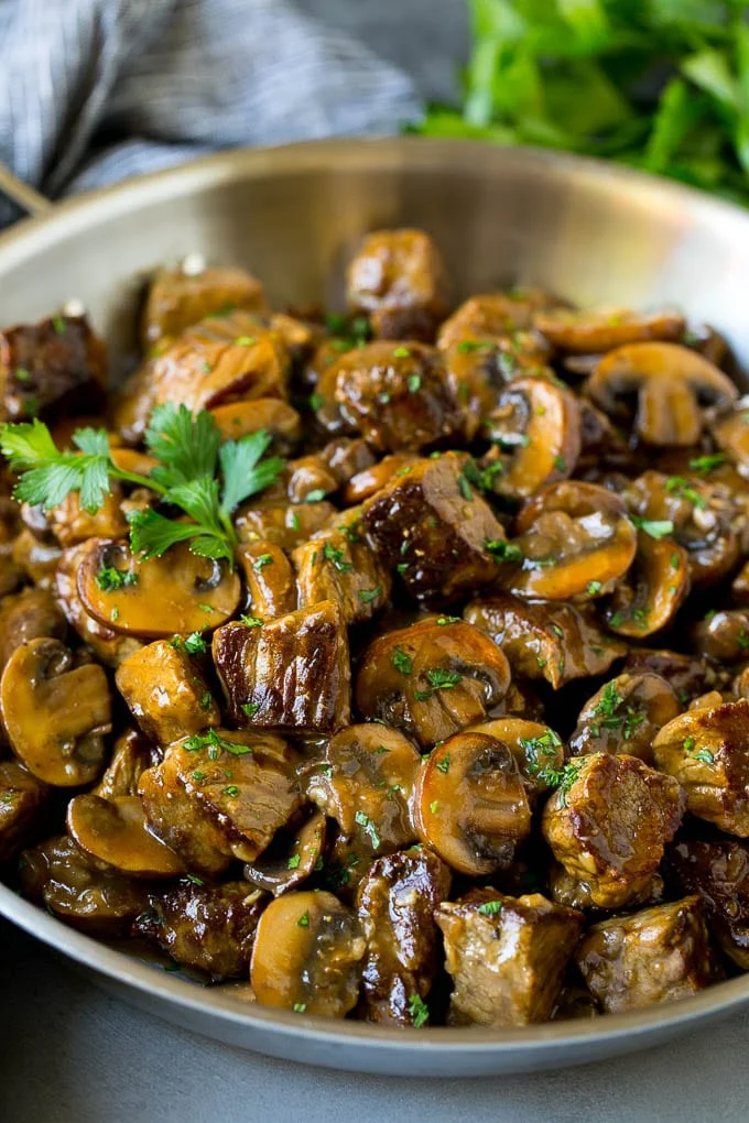 Plat mijoté de bœuf tendre aux champignons, garni de persil frais, servi dans une cocotte en fonte rustique.