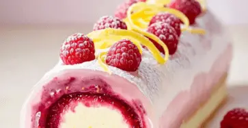 Bûche citron framboise décorée avec des zestes de citron, des framboises fraîches, et un glaçage brillant.