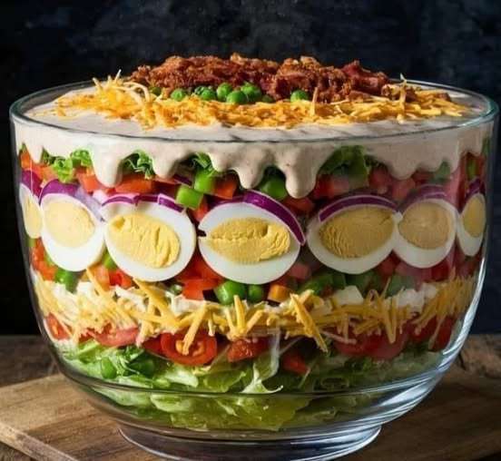 Salade à sept étages dans un bol en verre avec des couches colorées de légumes, œufs, cheddar et bacon