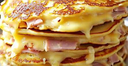 ancakes salés dorés, garnis de fromage fondu et morceaux de jambon, servis avec une salade verte et de la ciboulette fraîche