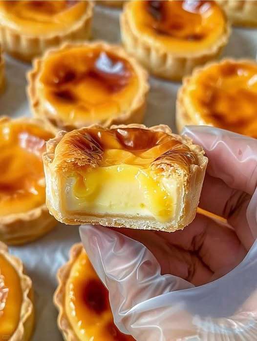 Pastéis de nata dorés et croustillants, garnis de cannelle et de sucre glace, disposés sur un plateau en bois avec une tasse de café à côté.