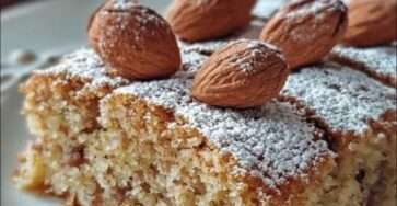 Un gâteau aux noisettes doré et moelleux, saupoudré de sucre glace, servi sur une assiette avec des noisettes entières en décoration.