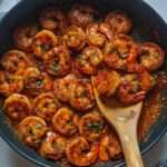 Crevettes sautées nappées d’une sauce épicée rouge, garnies de persil frais et servies avec du riz.