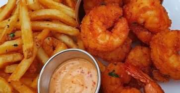 Crevettes frites dorées et croustillantes, servies avec une sauce épicée crémeuse et garnies de persil frais.