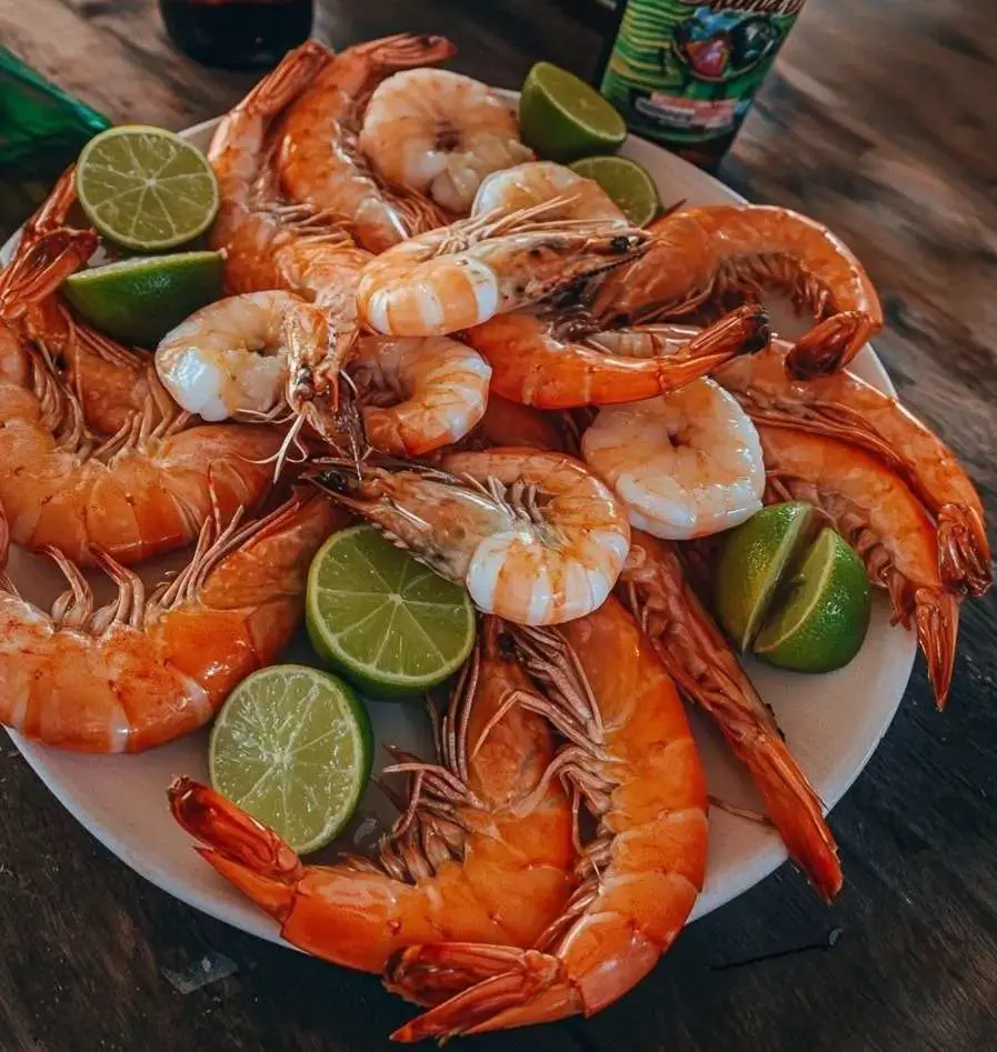 Crevettes bouillies, servies avec des quartiers de citron et de lime, garnies de persil frais.