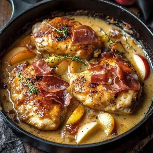 Poulet en sauce au cidre de pomme servi dans une assiette avec pommes et prosciutto croustillant.