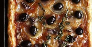 Photo d’une pissaladière dorée et croustillante, garnie d’anchois en croisillons et d’olives noires sur une pâte moelleuse.