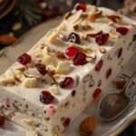 Nougat glacé maison aux amandes et fruits confits, servi en tranches sur une assiette avec un coulis de fruits rouges.