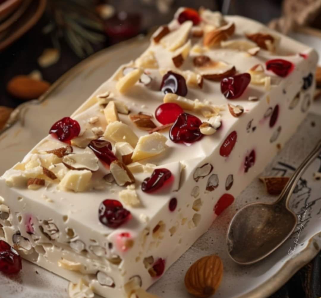 Nougat glacé maison aux amandes et fruits confits, servi en tranches sur une assiette avec un coulis de fruits rouges.