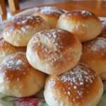 Petites brioches au yaourt dorées et moelleuses, servies sur une assiette avec un fond rustique en bois et un bol de confiture.