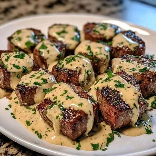 Trocitos de carne bañados en salsa cremosa de parmesano y ajo, decorados con perejil