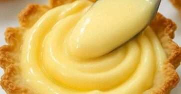 Crema pastelera casera servida en un bol de vidrio, con textura suave, rodeada de vainas de vainilla y ralladura de limón.