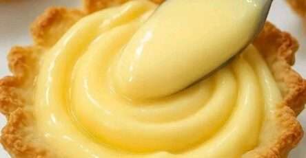 Crema pastelera casera servida en un bol de vidrio, con textura suave, rodeada de vainas de vainilla y ralladura de limón.