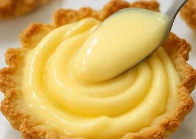 Crema pastelera casera servida en un bol de vidrio, con textura suave, rodeada de vainas de vainilla y ralladura de limón.