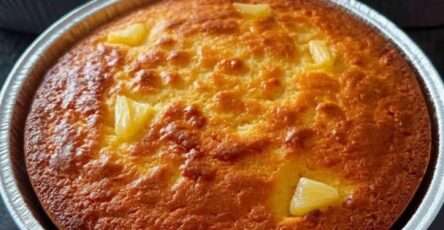 Rebanada de pan de elote cremoso con queso derretido encima, servida en plato blanco con una taza de café y fondo rústico de madera.