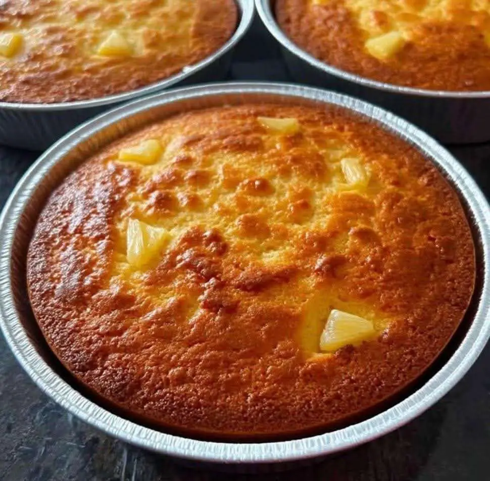 Rebanada de pan de elote cremoso con queso derretido encima, servida en plato blanco con una taza de café y fondo rústico de madera.