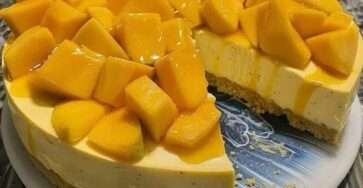 Pay frío de mango servido en una base de galleta, decorado con cubos de mango fresco y crema batida sobre una mesa veraniega.