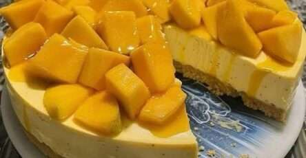 Pay frío de mango servido en una base de galleta, decorado con cubos de mango fresco y crema batida sobre una mesa veraniega.