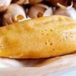 Tamales dulces de piña abiertos en hoja de maíz, mostrando su interior amarillo y trozos de piña, sobre una mesa rústica con taza de chocolate caliente.