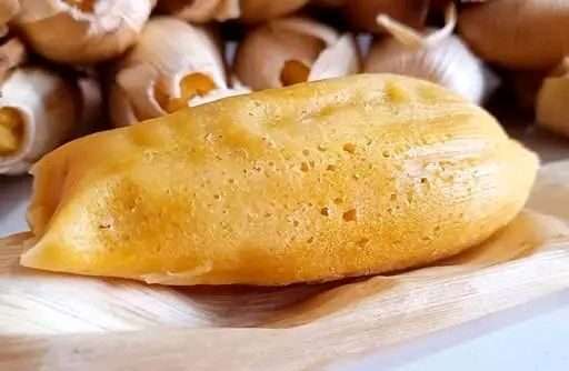 Tamales dulces de piña abiertos en hoja de maíz, mostrando su interior amarillo y trozos de piña, sobre una mesa rústica con taza de chocolate caliente.
