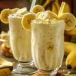 Batido cremoso de piña y banana servido en vaso con hielo, decorado con rodajas de fruta