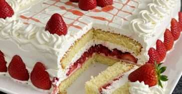 Pastel de fresa clásico redondo con crema batida y fresas frescas, decorado en la parte superior con frutas enteras y servido en una bandeja blanca.