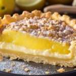 Tarte au citron à la croûte dorée et à la garniture lisse, surmontée de crème fouettée et zestes de citron